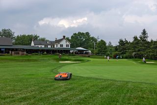 Tondeuse à gazon robotisée fonctionnant sur un terrain de golf avec des gens en arrière-plan.