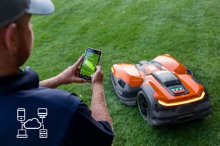 Eine Person, die ein Smartphone verwendet, um einen Mähroboter auf einem Rasen zu steuern, wobei Verbindungssymbole eingeblendet werden.