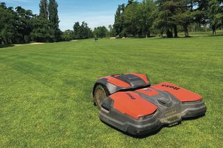 Robot tagliaerba in funzione in un grande giardino con alberi sullo sfondo.