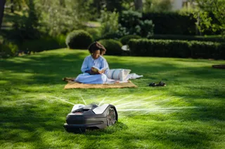 A robotic lawn mower operating on a well-maintained lawn with a person sitting in the background.