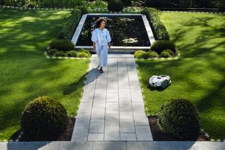A person standing on a paved path in a well-maintained garden with a water feature.