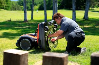 屋外で膝をついて、芝生の上でロボット芝刈機の下側を整備している人。
