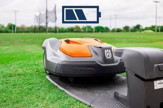 Robot-tondeuse Husqvarna à une station de charge sur un terrain d’herbe avec une icône de batterie superposée.