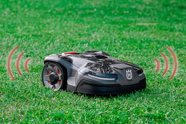Husqvarna robotic lawn mower on grass with wireless signal icons.