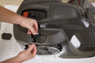 A person inserting a battery into a robotic lawn mower, showcasing the battery compartment.
