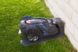 Mähroboter kehrt zu seiner Ladestation in einem Garten zurück, auf der sich Wassertropfen befinden.