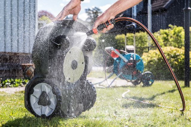 A person cleaning a robotic lawn mower with a hose in a garden setting.
