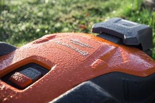 Close-up of a Husqvarna robotic lawn mower with morning dew on its surface.