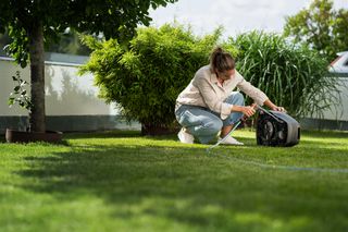 Een persoon die een robotmaaier reinigt in een tuinomgeving.
