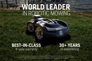 Robotic lawn mower on grass near a waterfront, promoting world leadership in robotic mowing.