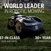 Robotic lawn mower on grass near a waterfront, promoting world leadership in robotic mowing.