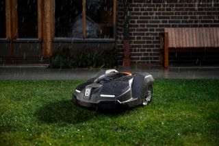 Robotic lawn mower operating on a grass lawn during rainfall.