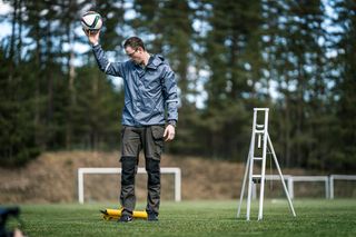 A person standing on a grassy field holding a soccer ball, with a ladder nearby.