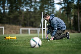 A person setting up a tripod on a soccer field with a soccer ball in the foreground.