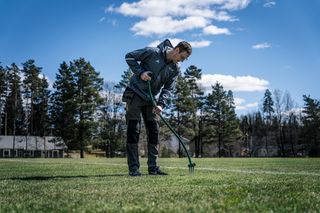 Ένα άτομο που χρησιμοποιεί ένα εργαλείο κήπου για να αερίσει ένα γκαζόν σε ένα πάρκο.