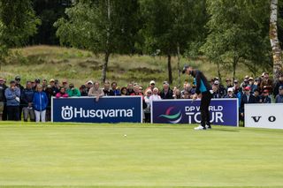 A golfer preparing to putt on a green during a tournament, with spectators and Husqvarna signage in the background.