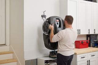 A person mounting a robotic lawn mower on a wall in a garage setting.
