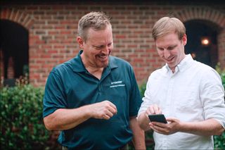 Two people discussing something on a smartphone in a garden setting.