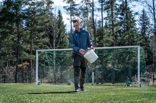 Ένα άτομο απλώνει σπόρους γρασιδιού σε ένα γήπεδο ποδοσφαίρου.