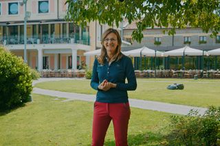 Una persona in piedi in un giardino con un robot tagliaerba che funziona sullo sfondo.
