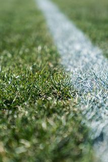 Κοντινή άποψη μιας λευκής γραμμής σήμανσης σε ένα χορταριασμένο αθλητικό γήπεδο.