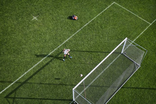 Une personne jouant au football, se préparant à frapper un ballon vers un but sur un terrain en herbe.