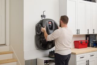 A person mounting a robotic lawn mower on a wall in a garage setting.