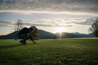 Une personne inspecte l’herbe dans un paysage pittoresque au coucher du soleil.