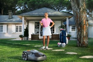 Robotic lawn mower on a garden lawn; person practicing putting near a house.