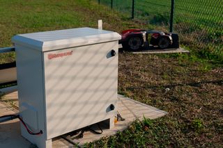 A Husqvarna robotic lawn mower charging station with a mower in the background on grass.