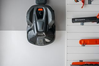 A Husqvarna robotic lawn mower mounted on a wall next to various Husqvarna gardening tools.