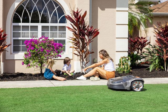 A robotic lawn mower operating near a family gardening in a residential yard.
