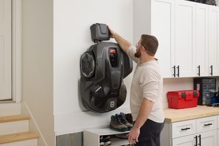 A person placing a robotic lawn mower on a wall-mounted storage in a garage.