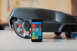 Een smartphone met verschillende apps naast een robotmaaier.