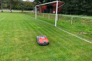 Robotic lawn mower operating on a football field near a goal post.
