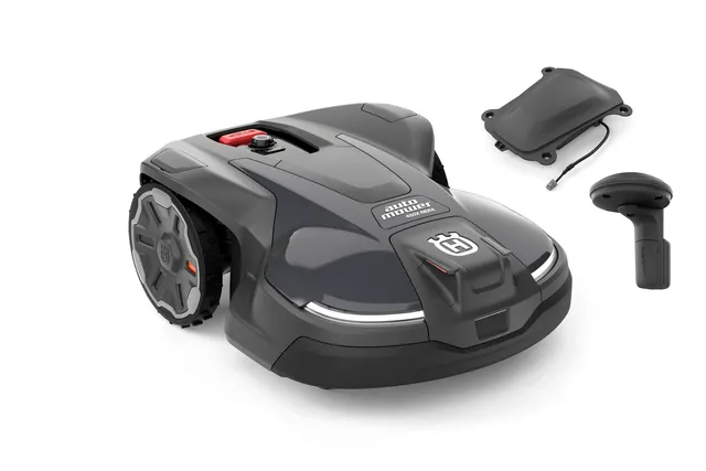 Front view of a Husqvarna robotic lawn mower with its charging station and remote control.