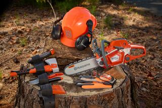 Un set di motosega Husqvarna, ascia, guanti ed elmetto di sicurezza con protezione acustica su un ceppo d'albero.