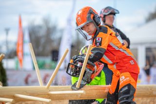 Person using a Husqvarna chainsaw to cut a log during an outdoor competition.