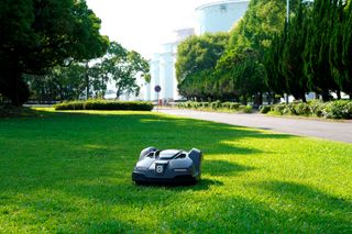 木々や建物の近くの芝生で稼働するロボット芝刈り機。
