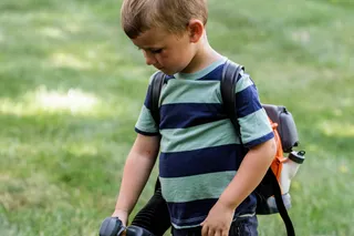 A child using a leaf blower to clear bubbles on a grassy area.
