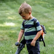 A child using a leaf blower to clear bubbles on a grassy area.