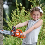 A child holding a Husqvarna toy chainsaw in a garden setting.