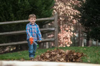 A child walking in a garden with a toy leaf blower near a pile of leaves.