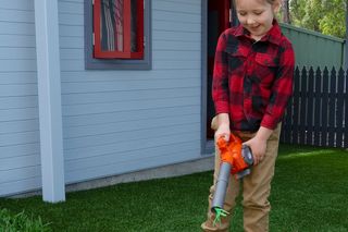 Et barn som bruker en løvblåser til å fjerne løv fra en plen i en bakgård i et boligområde.