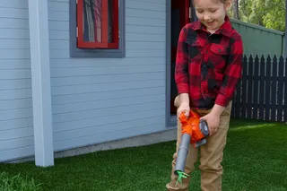 A child using a leaf blower to clear leaves from a lawn in a residential backyard.