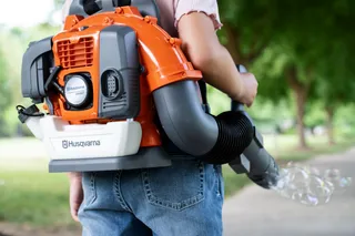 A person using a Husqvarna backpack leaf blower in a park setting.