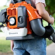 A person using a Husqvarna backpack leaf blower in a park setting.