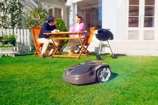 近くのテーブルに2人が座っている間、庭で稼働するロボット芝刈り機。