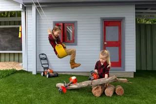 Two children playing in a garden with toy lawn mowers and logs.