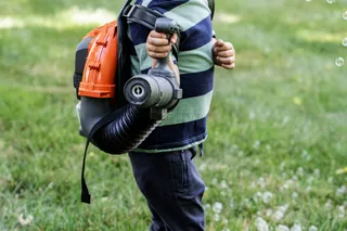 A child holding a leaf blower in a grassy area.